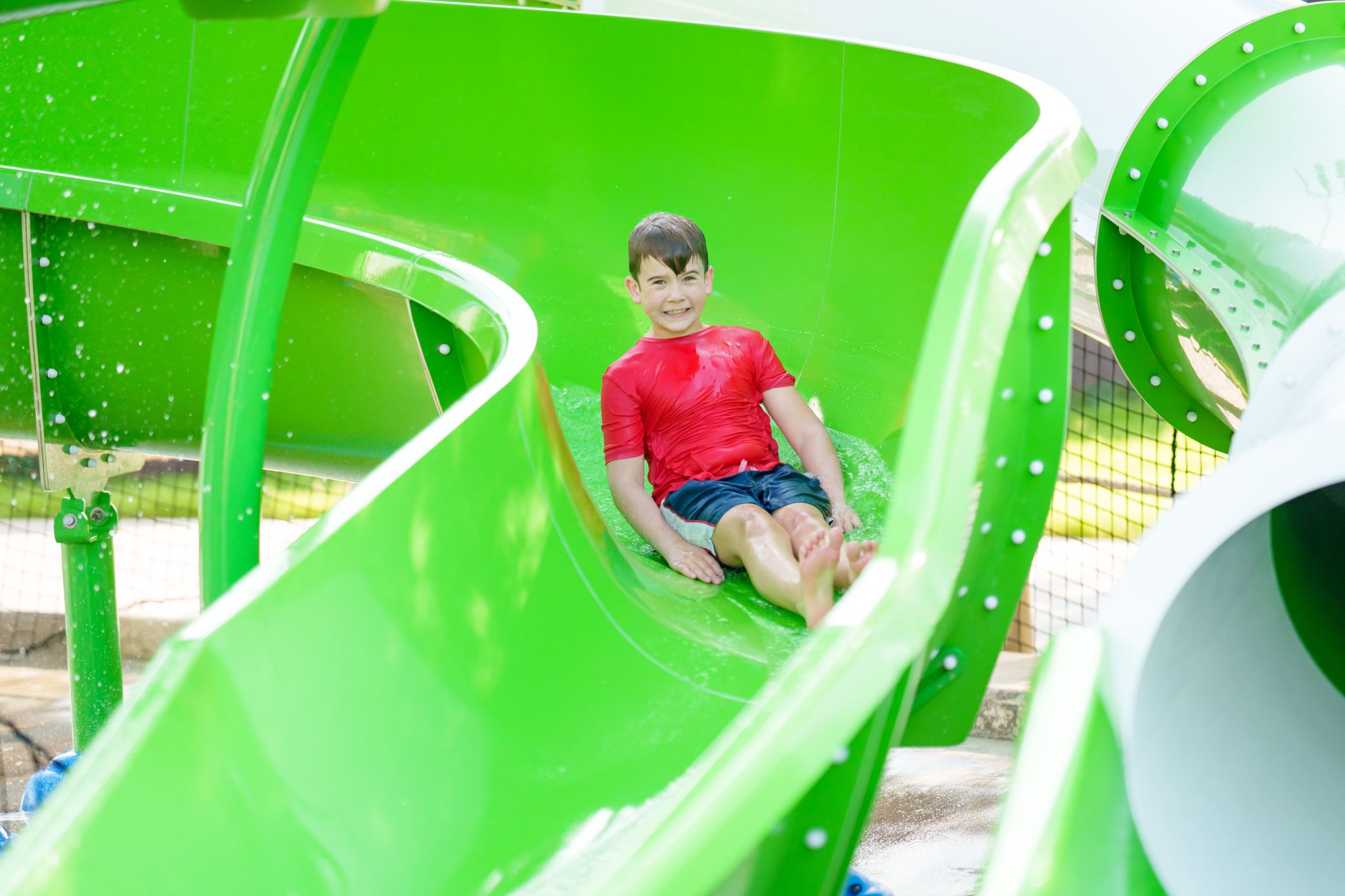 Child sliding down water slide on Bahama Beach Waterpark's Elevations aquatic play structure with colorful waterslides in Dallas, Texas