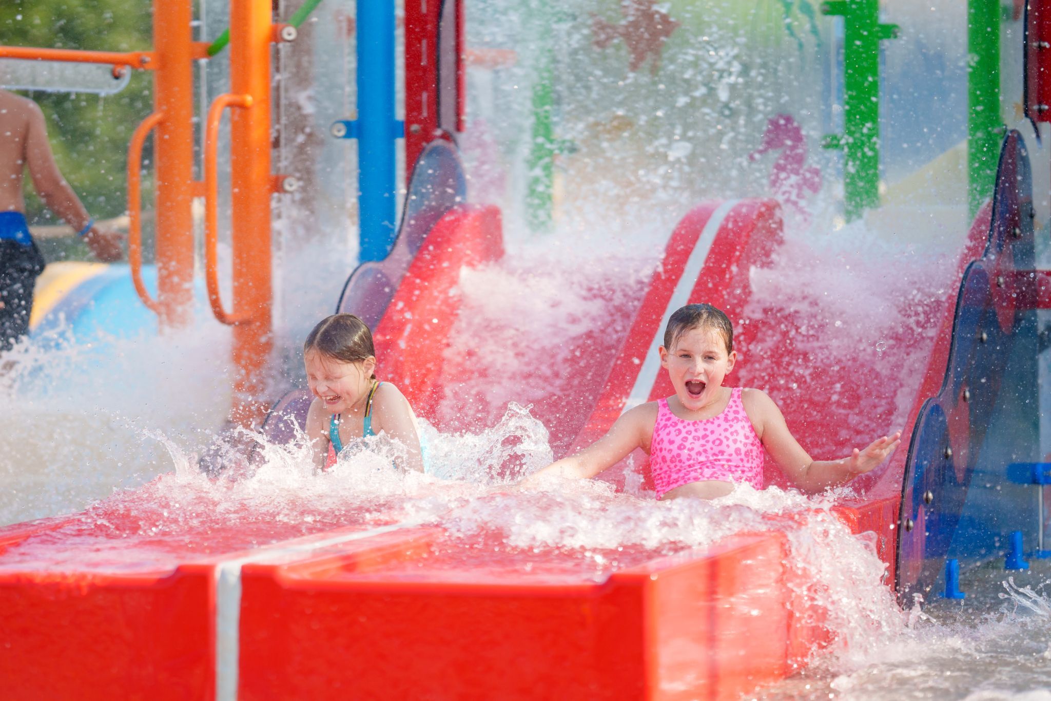 Children sliding down water slide on Bahama Beach Waterpark's Elevations aquatic play structure with colorful waterslides in Dallas, Texas