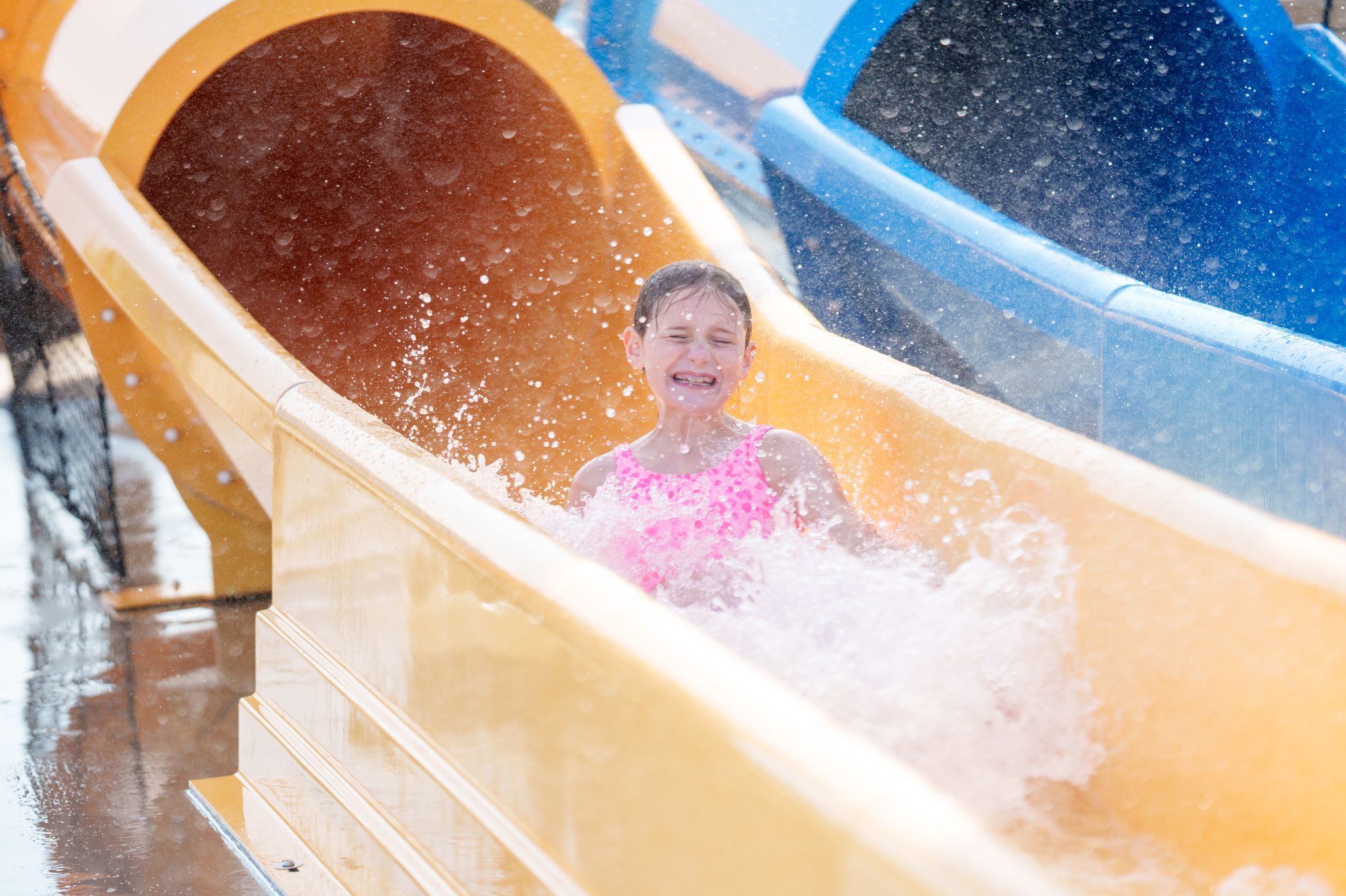 Child sliding down water slide on Bahama Beach Waterpark's Elevations aquatic play structure with colorful waterslides in Dallas, Texas