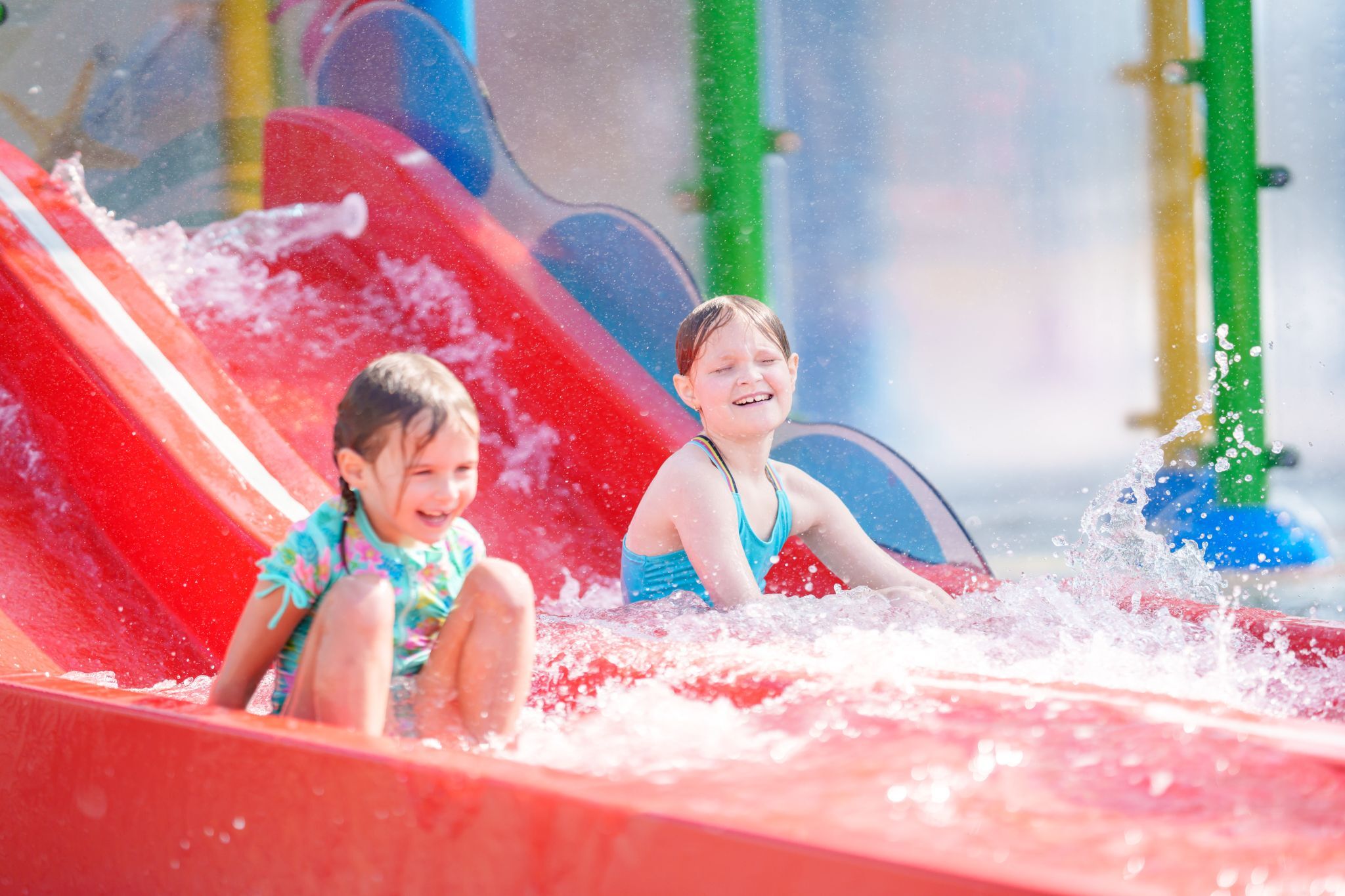 Child sliding down slide on Bahama Beach Waterpark's Elevations aquatic play structure with colorful waterslides in Dallas, Texas