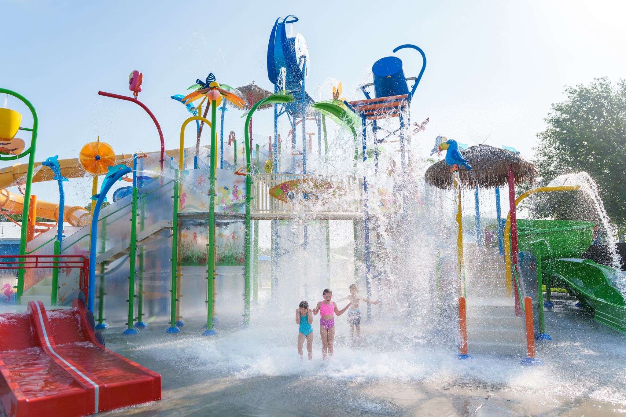 Children under splashing water at Bahama Beach Waterpark's Elevations aquatic play structure with colorful waterslides in Dallas, Texas