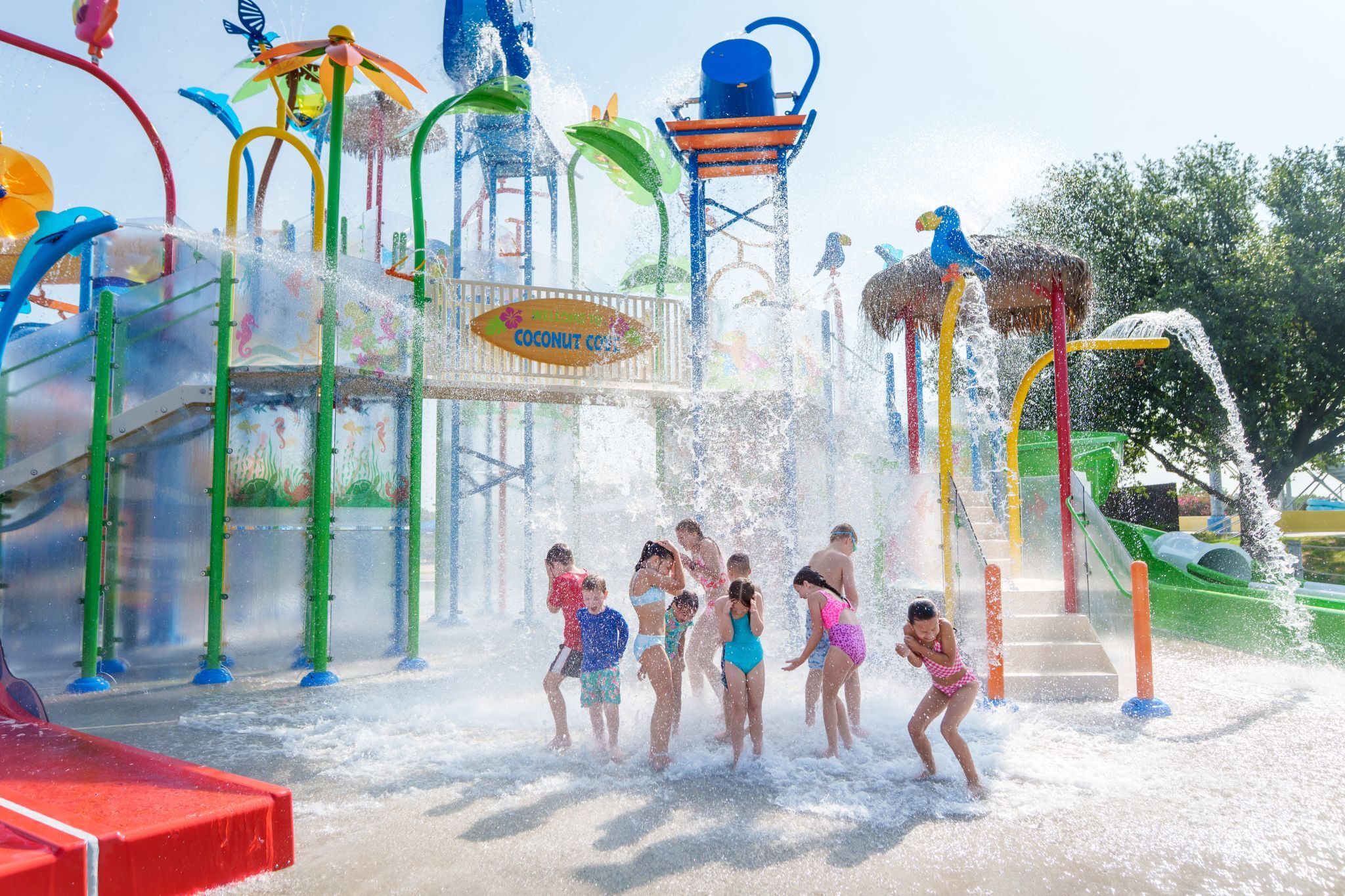 Children playing under water splash at Bahama Beach Waterpark's Elevations aquatic play structure with colorful waterslides in Dallas, Texas