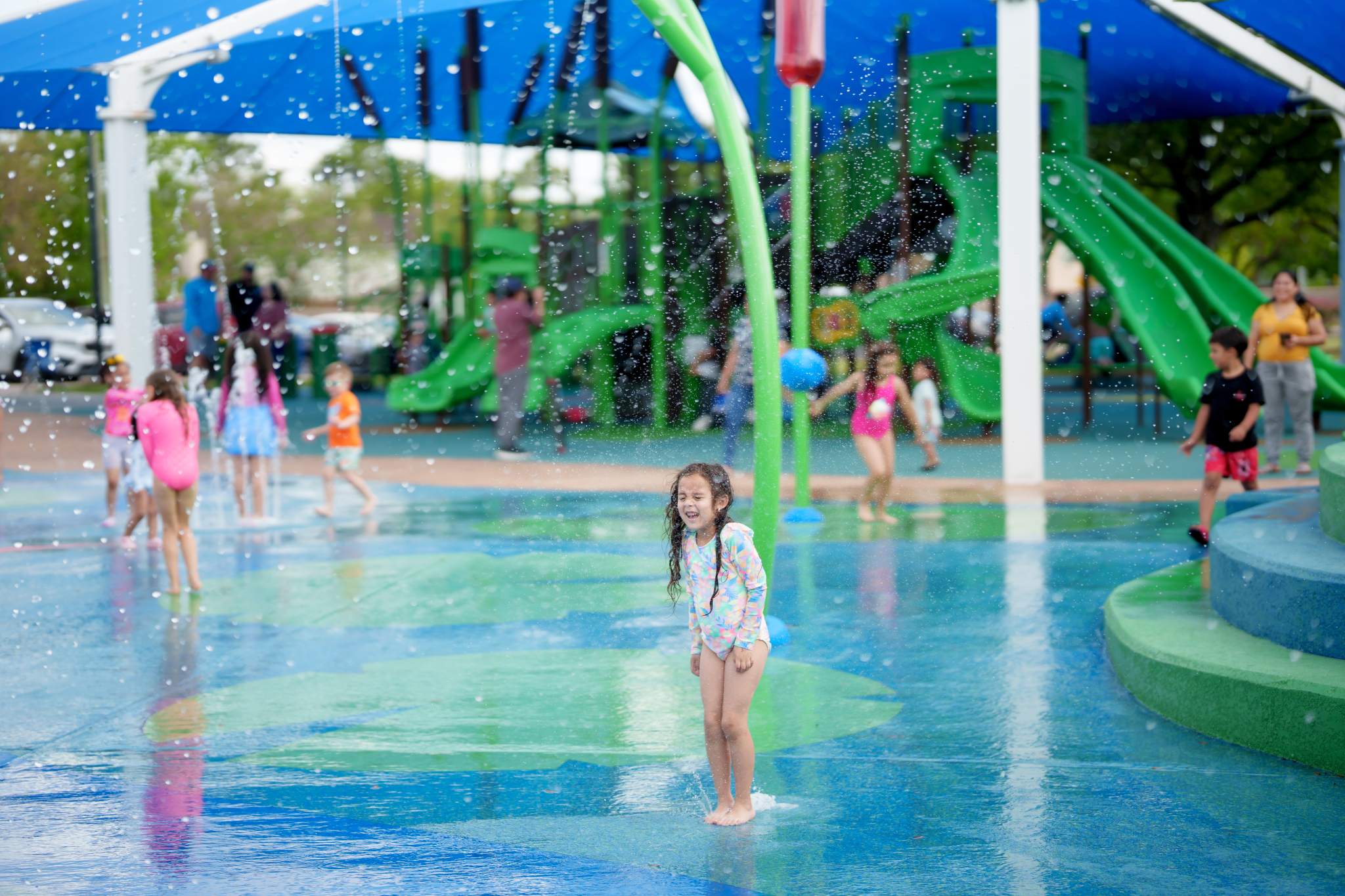 Child playing in splash pad with playground in the background